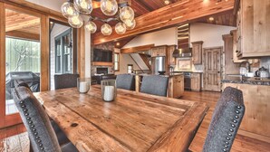 A spacious dining area with a wooden table and chairs, a chandelier, and a view of the kitchen and living area. - Modern Mountain Luxury Home, Game Room! 8-Person Private Hot Tub (Park City)