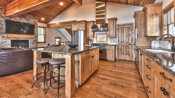 A spacious kitchen with wooden beams, a stone fireplace, a large island with stools, and modern appliances. - Modern Mountain Luxury Home, Game Room! 8-Person Private Hot Tub (Park City)