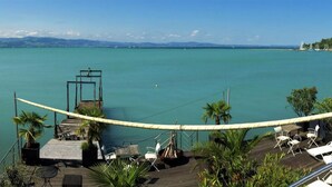 A wooden deck with outdoor seating, overlooking a calm body of water with a distant shoreline. - Pension Am Bodensee (Kressbronn)