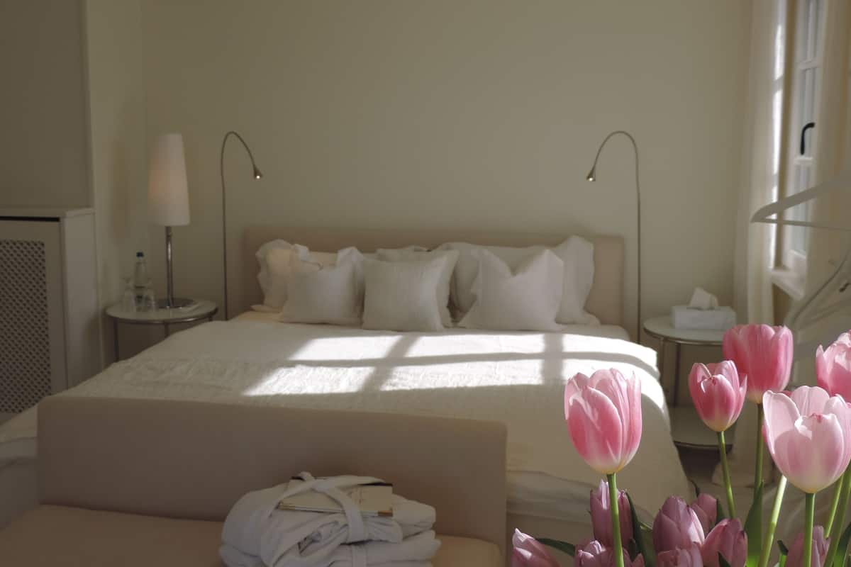 A hotel room with a bed, bedside tables, a lamp, and a window with natural light.