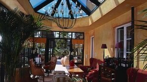 A spacious room with a high ceiling, a chandelier, and a large window providing natural light. There are multiple seating areas with chairs and a sofa, and a dining table with chairs. - Pension Am Bodensee (Kressbronn)