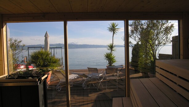 A wooden deck with outdoor furniture overlooking a lake, with mountains in the background. - Pension Am Bodensee (Kressbronn)