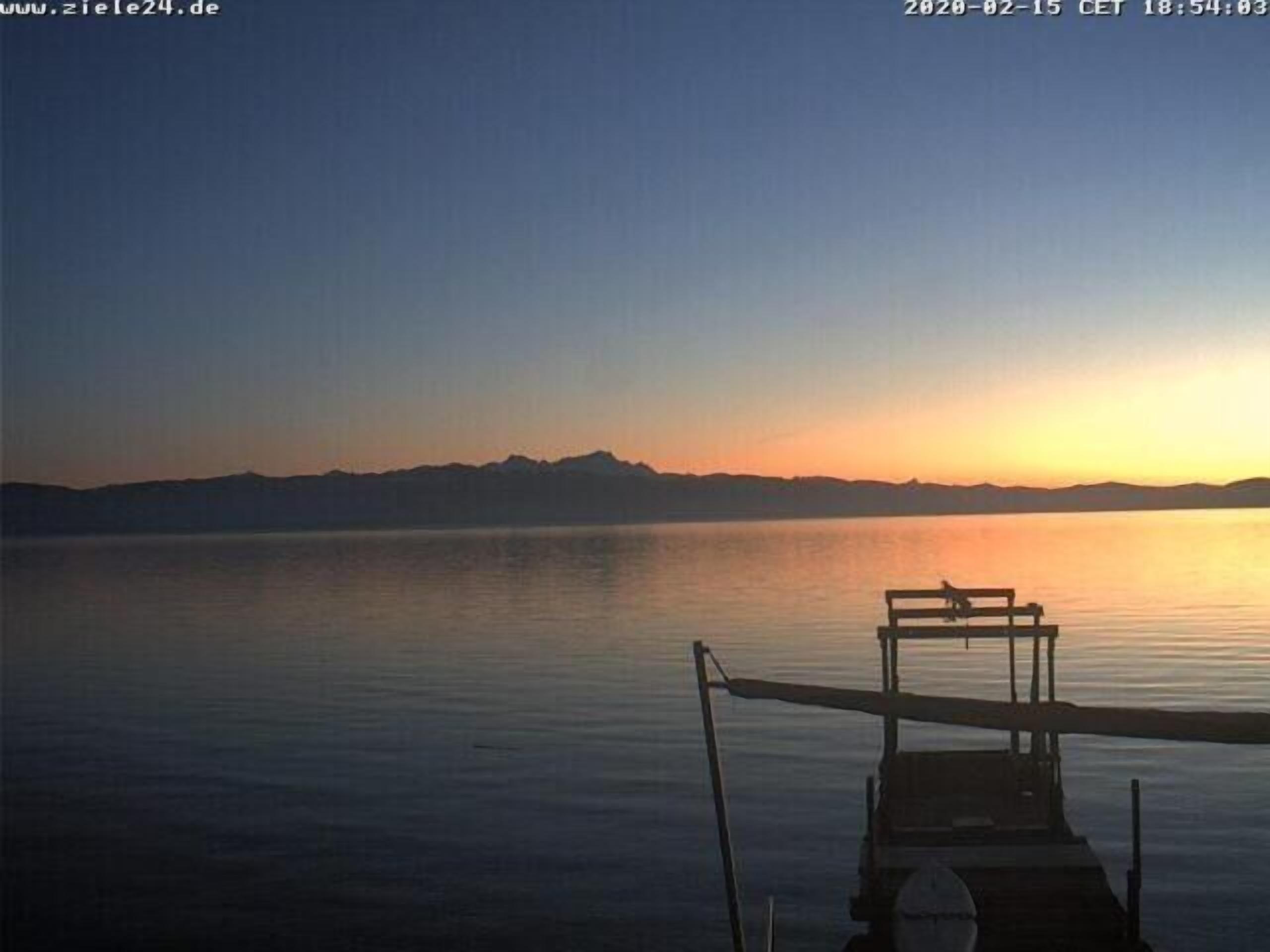Un lago tranquilo al atardecer con un muelle y un banco.