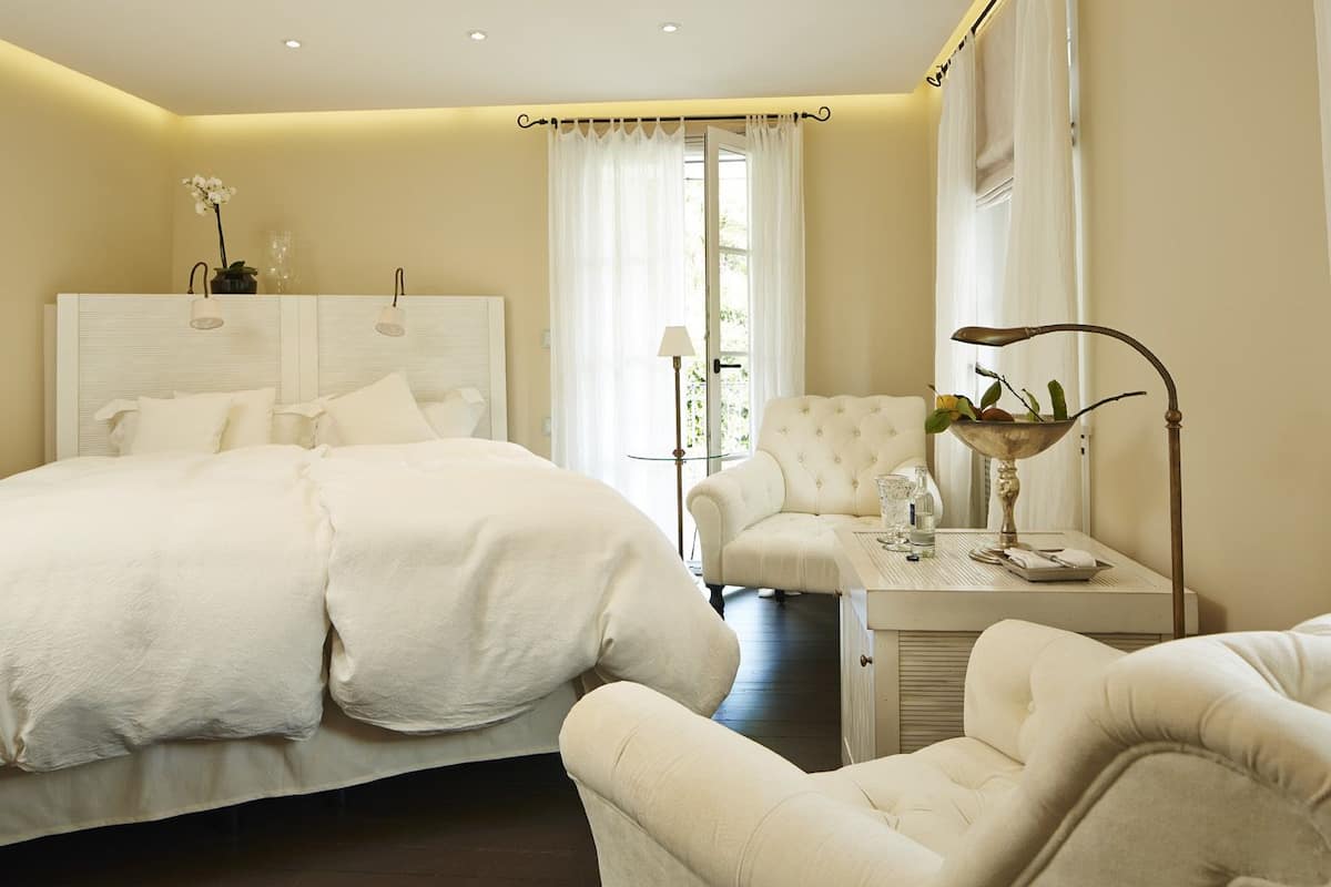 A hotel room with a large bed, a sitting area with a table, and a window with curtains.