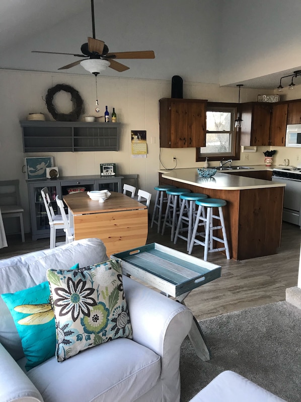 A cozy kitchen with wooden cabinets, a central island with stools, a dining table with chairs, and a ceiling fan.