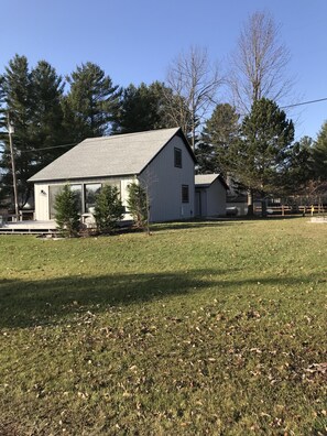 A white single-story house with a sloped roof, surrounded by a grassy yard and trees.