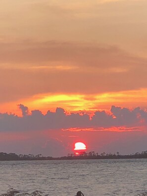 Un coucher de soleil sur une étendue d’eau, avec une silhouette de terre visible au loin.