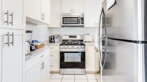 A compact kitchen with white cabinets, a stainless steel stove, a microwave, and a refrigerator. - Ground Level Home With Deepwater Canal And 30' Of Dock Space (Summerland Key)