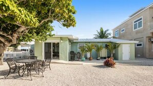 A building with a covered patio, outdoor seating, and potted plants. - Ground Level Home With Deepwater Canal And 30' Of Dock Space (Summerland Key)