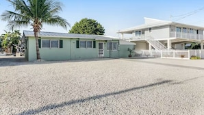 A two-story building with a green facade, a palm tree in front, and a gravel driveway. - Ground Level Home With Deepwater Canal And 30' Of Dock Space (Summerland Key)