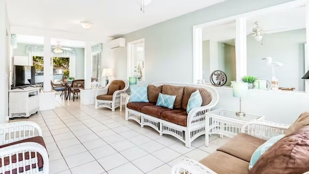 A spacious living area with white wicker furniture, a brown sofa with blue cushions, and a large mirror. - Ground Level Home With Deepwater Canal And 30' Of Dock Space (Summerland Key)
