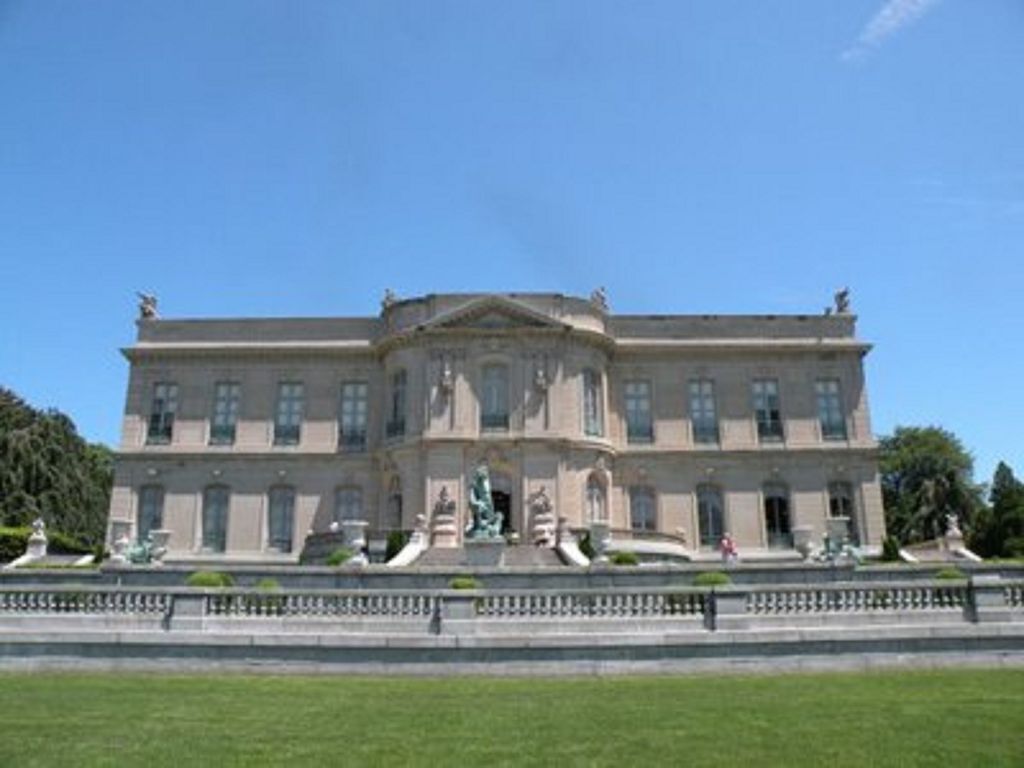 A large, classical building with a symmetrical facade, a central entrance with statues, and a well-maintained lawn in the foreground.
