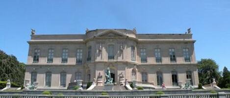 A large, classical building with a symmetrical facade, a central entrance with statues, and a well-maintained lawn in the foreground.