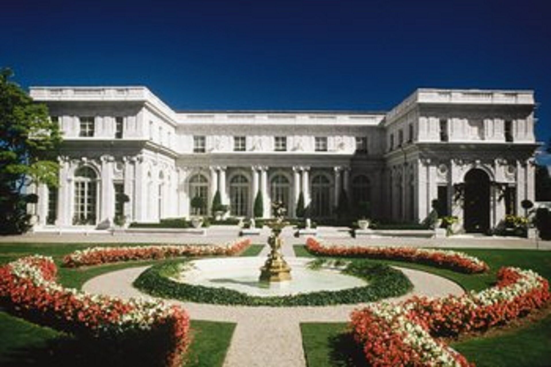 A large, classical building with symmetrical architecture, a central courtyard with a fountain, and formal landscaping.