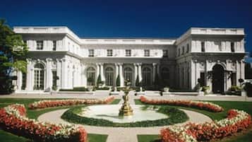 A large, classical building with symmetrical architecture, a central courtyard with a fountain, and formal landscaping.