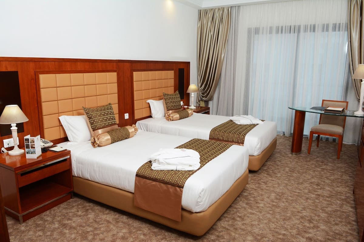 A hotel room with two beds, a desk, a chair, and a small table.