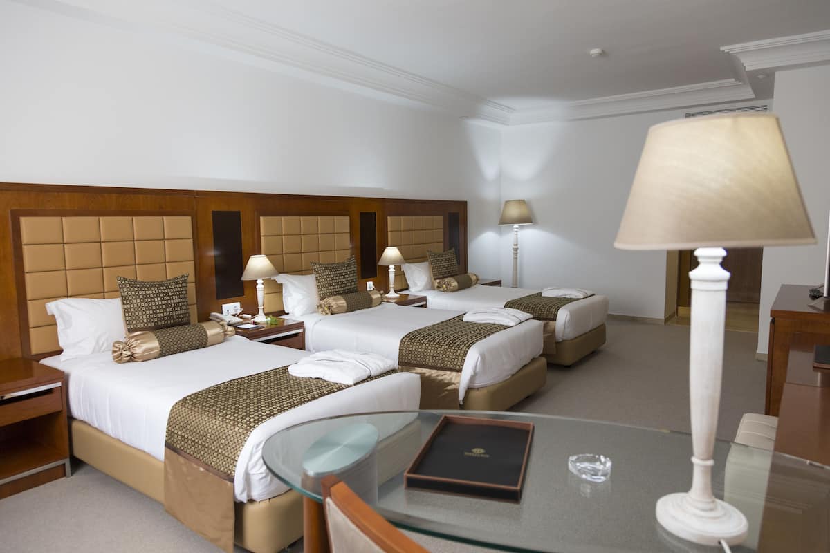 A hotel room with two beds, a glass table, and a lamp.