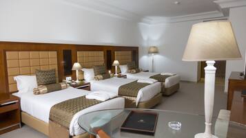 A hotel room with two beds, a glass table, and a lamp.