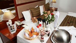 A neatly arranged hotel room with a bed, bedside table, and a dining area with a table set for two. - Marigold Hotel (Tunis)