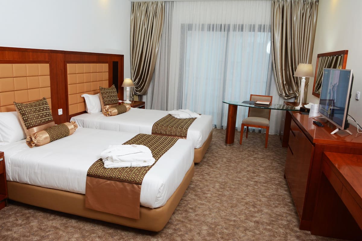 A hotel room with two beds, a desk, a chair, a TV, and curtains.