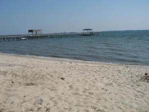 A beach with a wooden pier extending into the water, featuring two covered structures. - Quiet Riverfront House with Private Sandy Beach. Close to Colonial Williamsburg. (Hayes)