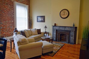 A living room with a brick wall, a fireplace, a sofa set, a small table, and a clock on the wall.