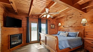 Ein Schlafzimmer einer Holzhütte mit einem Bett, einem Fernseher, einem Kamin und einem Deckenventilator.
