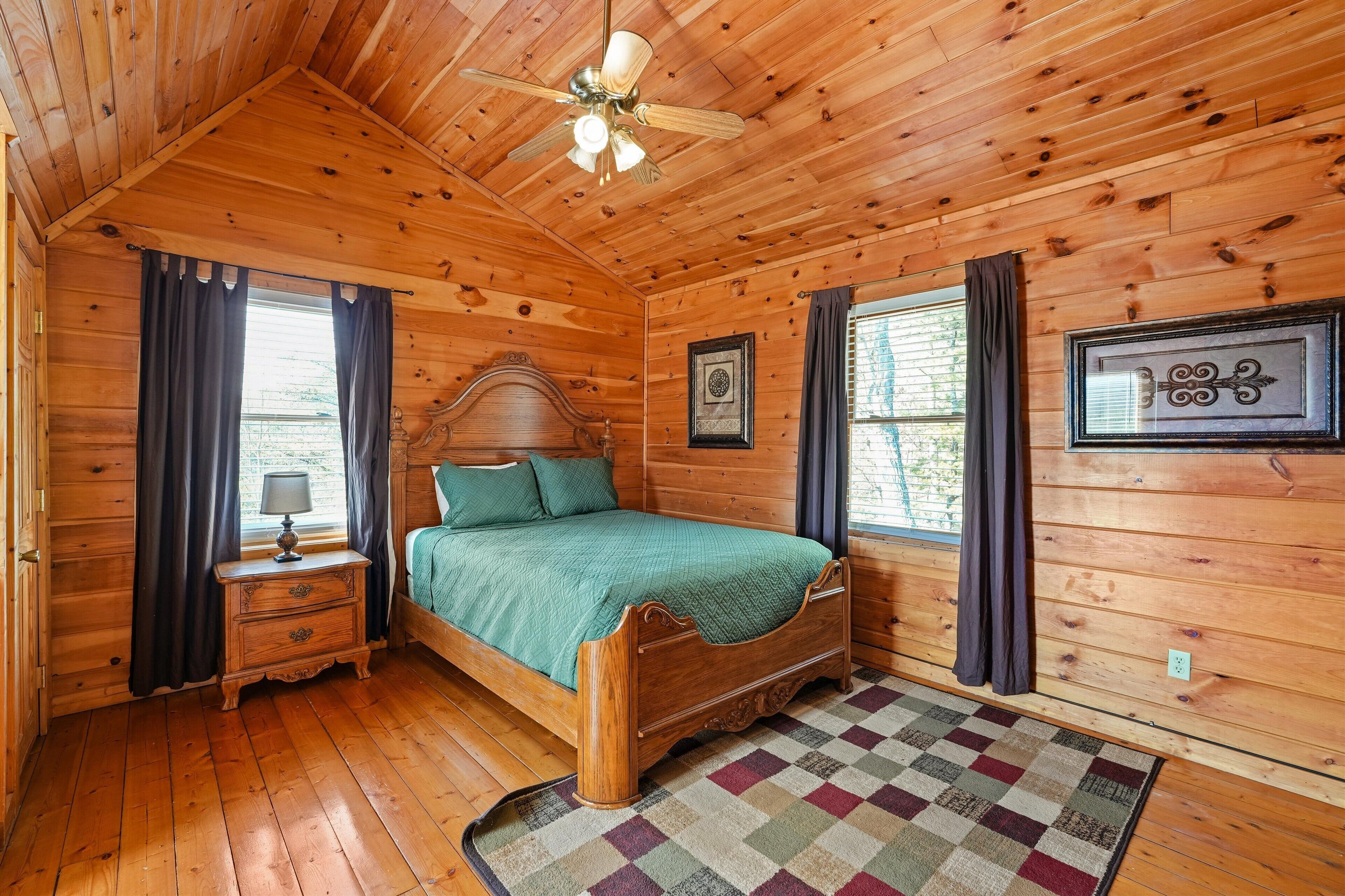 Quarto de cabana de madeira com cama, mesa de cabeceira e ventilador de teto.