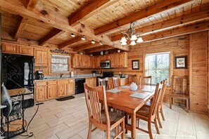 Una cabaña de madera con cocina, que incluye una mesa de comedor, sillas y varios electrodomésticos.