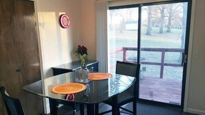 A dining area with a glass table, black chairs, and a wooden deck visible through the glass door.