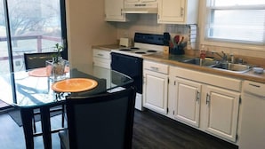 A kitchen with white cabinets, a stove, and a sink. There is a glass table with chairs and a window providing natural light.