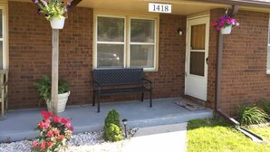 A brick building with a porch, a bench, and hanging flower baskets.