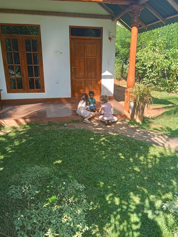 A house with a wooden door and windows, a porch, and a garden with greenery. - Green View Safari Resort (Udawalawa)