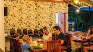 Un restaurante con mesas y sillas de madera, un muro de ladrillo con motivos de hojas verdes y una puerta que da al exterior.
