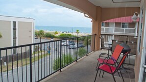 A balcony with a view of the beach, a barbecue grill, and a red chair. - Brass Rail 3 Bed, 2.5 Bath Ocean View Top Floor Closest To Beach (Tybee Island)
