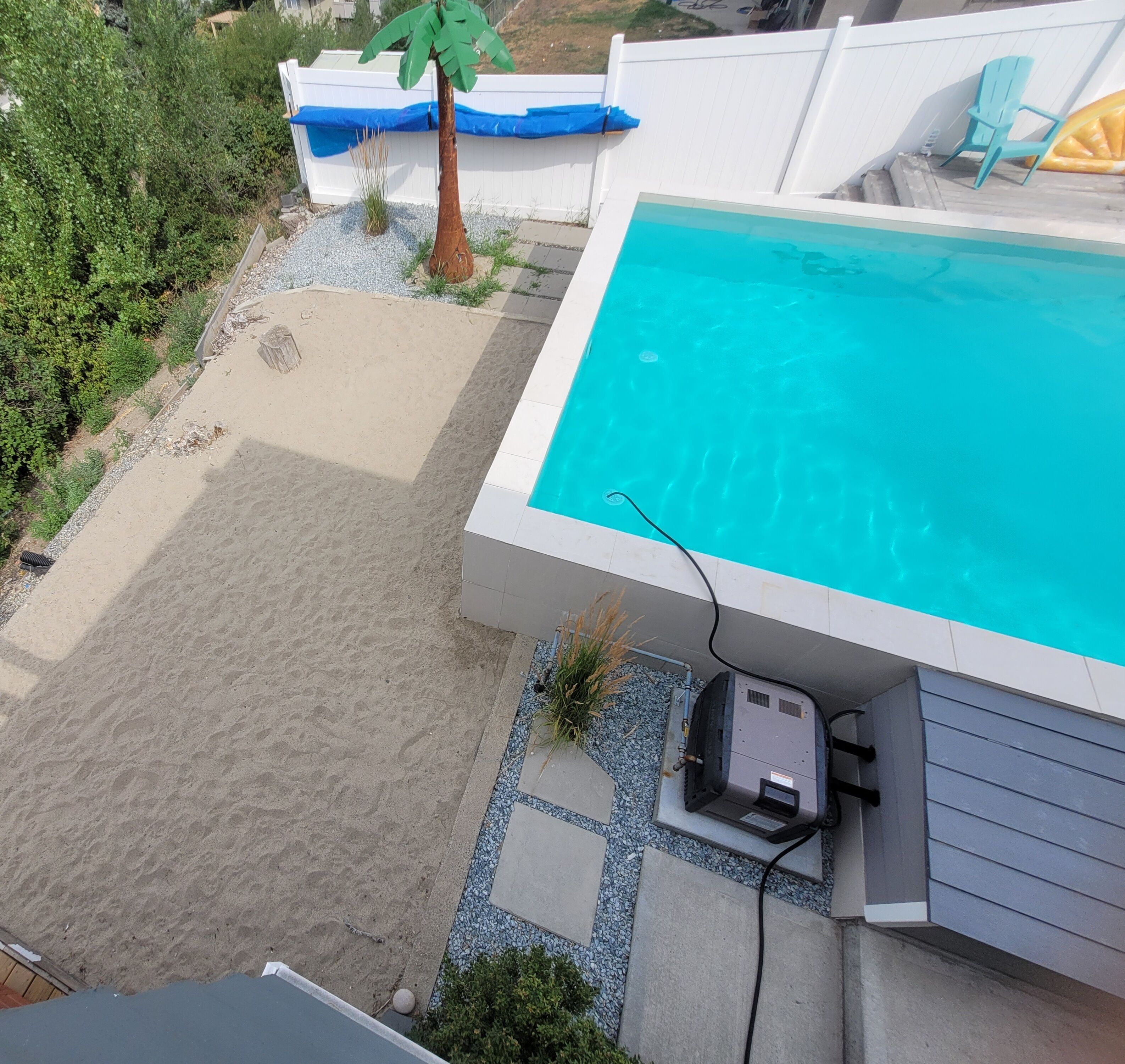 A swimming pool with a sandy area and a small garden.