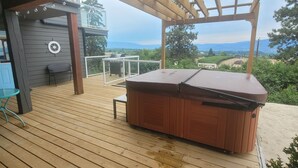 A wooden deck with a hot tub, a table, and a chair. -   FULLY LICENCED : Private HEATED POOL and hot tub with Okanagan valley view (Kelowna)