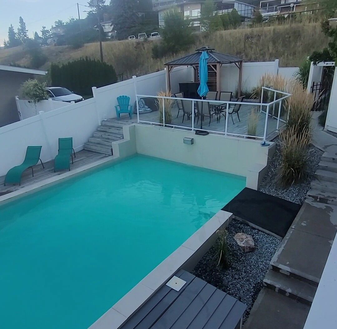 A backyard with a swimming pool, a covered patio area, and a few lounge chairs.