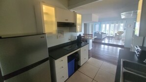 Una cocina moderna con refrigerador, estufa y lavamanos. Hay un comedor con mesa y sillas. La habitación tiene ventanas amplias y vistas al exterior.