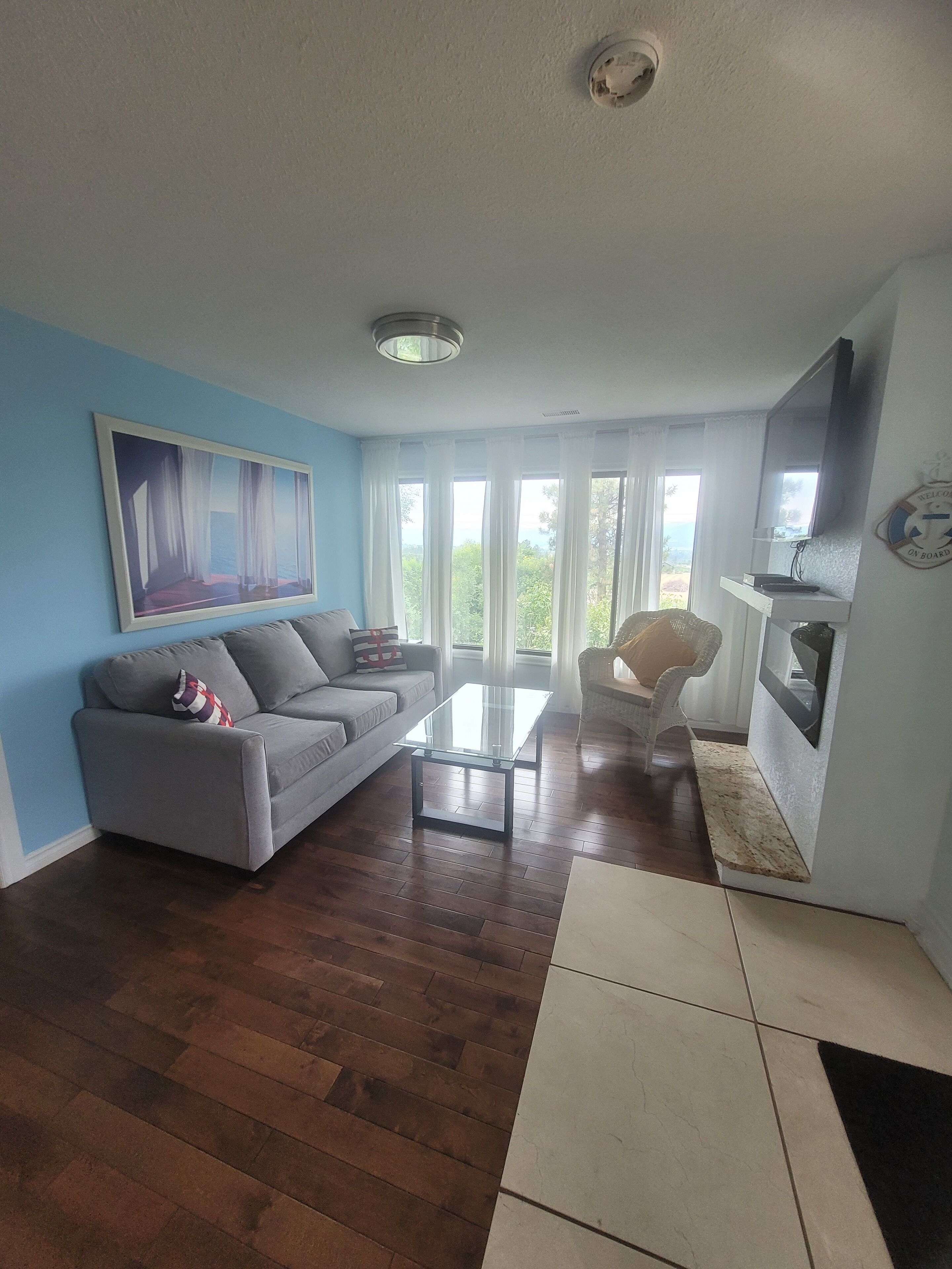 A living room with a sofa, a glass coffee table, a chair, and a television mounted on the wall.