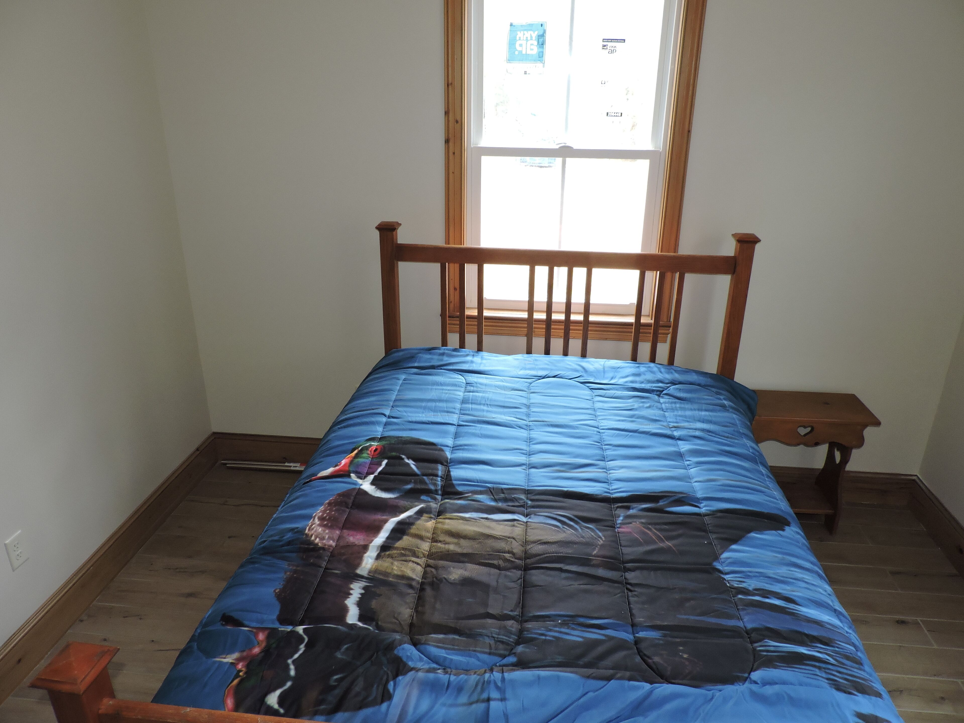 Una cama con un edredón azul en una habitación con cabecera de madera, un pequeño banco de madera y una ventana con vistas al exterior.