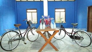 A room with blue walls, two bicycles, a wooden table, and a window with bars. - Reef Pasikudah (Nasuvantivu)
