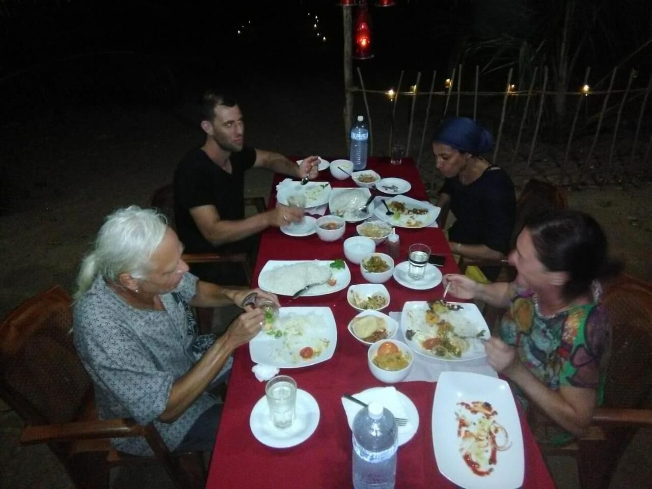 Un grupo de personas cenando en una mesa al aire libre, con diferentes platos y bebidas.