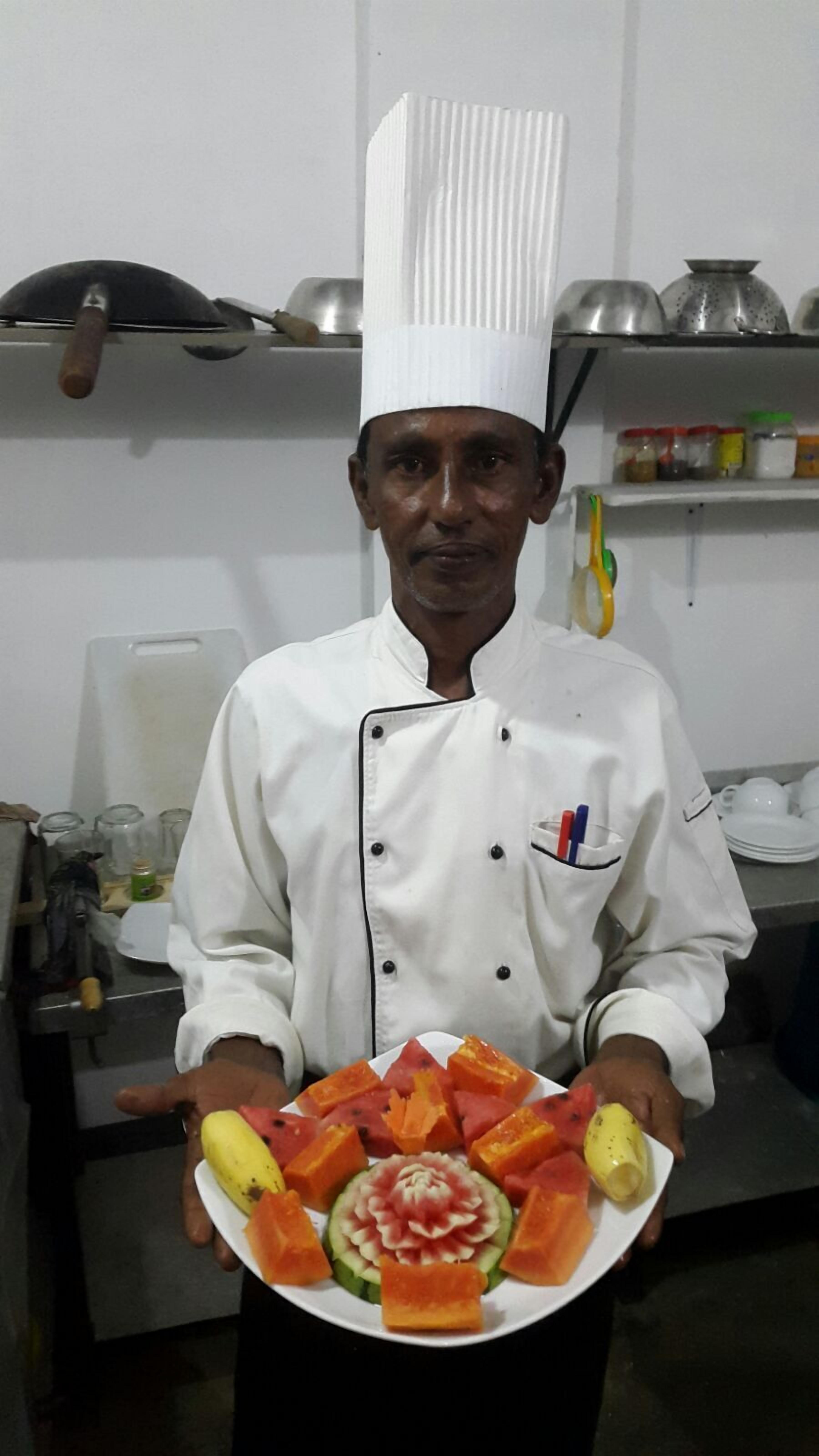 A chef in a white uniform holding a plate of carved fruits and vegetables.