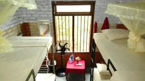 A dormitory room with two beds, a small table with a fan, and a window with bars. - Reef Pasikudah (Nasuvantivu)
