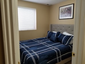 A bedroom with a bed, a window with blinds, a framed picture on the wall, and a door. - Your Clearfield home (Clearfield)