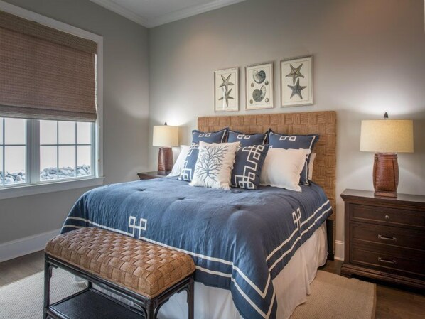 A bedroom with a bed, two bedside tables, a bench, and a window with blinds.