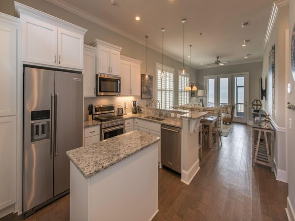 A modern kitchen with white cabinetry, stainless steel appliances, and a granite countertop island.