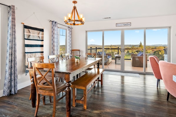 A dining area with a wooden table and chairs, a chandelier, and a view of a balcony with outdoor seating.