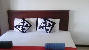 Una cama bien tendida con una colcha roja, dos almohadas con un diseño geométrico y una almohada azul.